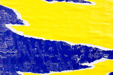 Yellow and blue old ripped paper posters and placards with dirty traces of glue on billboard.