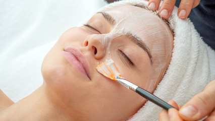 Close up of cosmetologist applies facial clay mask on an young beautiful woman face before...
