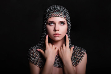 Portrait of a beautiful, young girl in a chainmail hood on a black background. Model with clean skin.