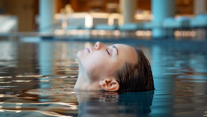Portrait of an young smiling woman is enjoying and having relax in a indoor swimming pool in a...