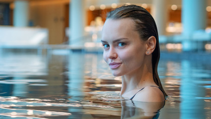 Portrait of an young smiling woman is enjoying and having relax in a indoor swimming pool in a luxury wellness center.