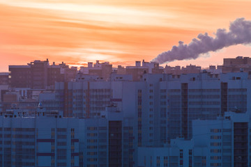The buildings of the new district or block and steam of the electric power station on the background of setting or rising sun in the morning or in the evening in the cold winter weather