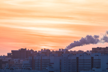 The buildings of the new district or block and steam of the electric power station on the background of setting or rising sun in the morning or in the evening in the cold winter weather