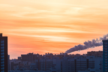 The buildings of the new district or block and steam of the electric power station on the background of setting or rising sun in the morning or in the evening in the cold winter weather