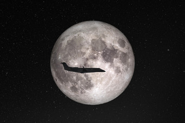Silhouette of private jet plane flying against background of huge full moon in dark starry space. Elements of this image furnished by NASA