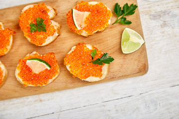Salmon red caviar in bowl and Sandwiches with on wooden cutting board on white background copy space.