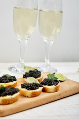 Sandwiches with black caviar. Sturgeon black caviar in wooden bowl, sandwiches and champagne on white background copy space.