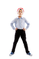 Smiling standing schoolboy in santa claus hat. Full height. Christmas mood. Isolated over white background. Vertical.