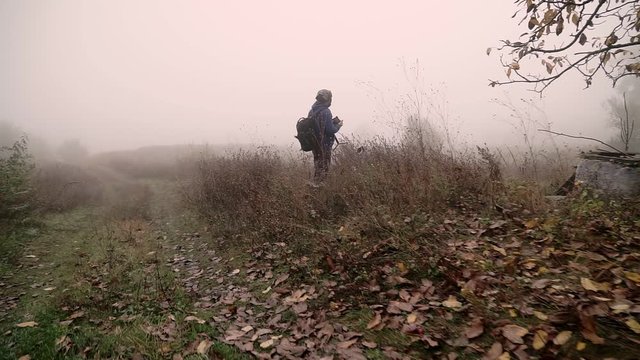 Male photographer taking photos in creepy foggy forest. Gloomy autumn rainy day