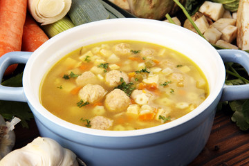 Broth with marrow dumplings and carrots, onions various fresh vegetables in a pot - colorful fresh clear spring soup. Rural kitchen scenery bouillon