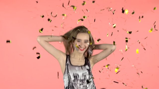 Girl posing with falling confetti in studio. Pink background. Slow motion