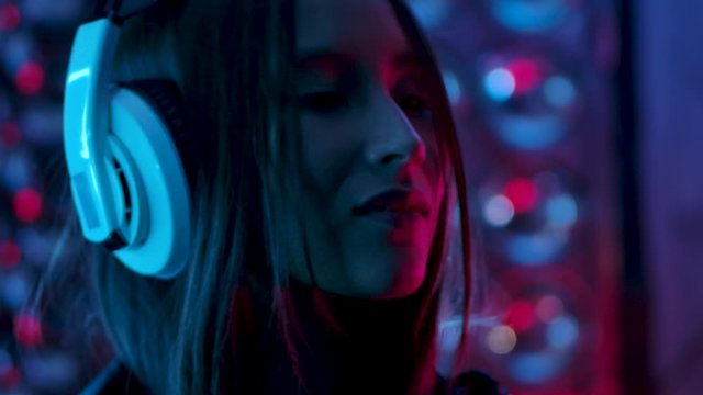 Portrait of 30s Alone Girl Who Listening Music in Earphones mp3 Player and Dancing on Party Enjoy Evening Slow Motion. Attractive Woman Looking at Camera Indoors with Colorful Purple Light CloseUp 4K
