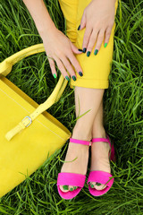 Green manicure and pedicure on the nails of the feet in pink sandals.Girl in yellow pants and bag...