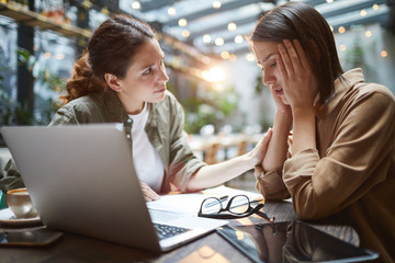 Side view portrait of frustrated young woman working at table in cafe with friend or colleague...