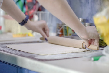 Obraz na płótnie Canvas Woman rolls puff pastry with a wooden rolling pin on a silicone mat for dough. The process of cooking baking.