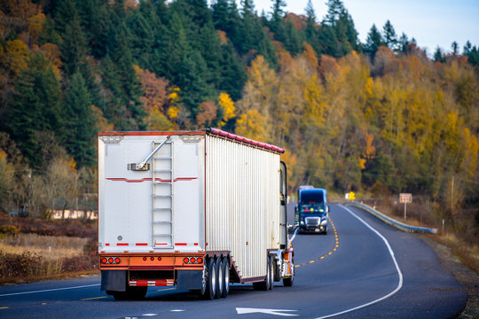Big rig semi truck with covered bulk semi trailer driving on the winding autumn road кгттштп towards another semi truck