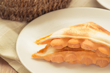 Sandwich stuffed with cheese and sausage in white dish on wooden table.