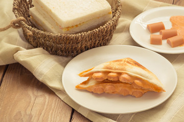 Sandwich stuffed with cheese and sausage in white dish on wooden table.