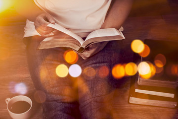 Close up of woman hands hold and reading bible indoor near a cup of coffee and book stack with...