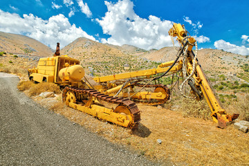 Tracked bulldozer with drilling machine at work along road. Work in progress, industrial machine. Mining landscape on background.