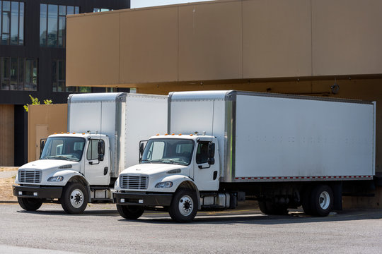 Small compact rigs semi trucks with long box trailers standing in warehouse dock loading cargo for delivery