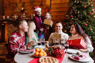 Father and daughter celebrate new year holidays with friends sitting at the table give each other gifts