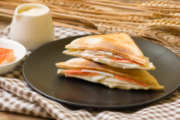 Sandwich stuffed with salad sauce and crab stick in black dish on wooden table.