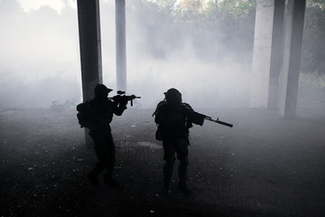 Two military soldiers in camouflage with assault rifles storming enemies in the gloom in the fog