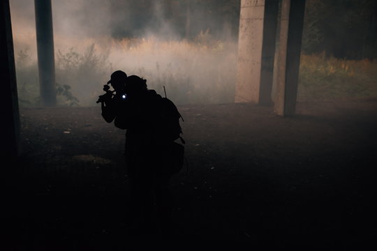 Two military soldiers in camouflage with assault rifles storming enemies in the gloom, forest fire. Storming the building with terrorists