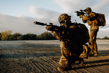 Two military soldiers in camouflage with assault rifles looking through the scope preparing to...