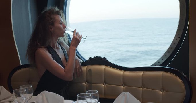 Beatiful woman is sitting alone at table in restaurant on cruise ship, drinking champagne.