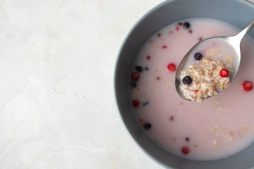 Close-up spoon with oat, berry and milk in gray bowl at breakfast on marble table background with copy space. Above