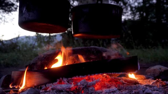 A close-up of two metal outdoor boilers over a campfire in the evening. 4k footage.