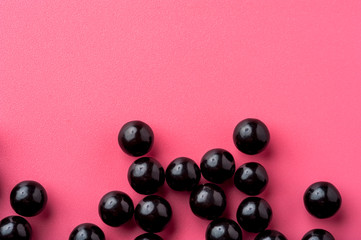 Close-up of black shiny pills lie on a pink surface