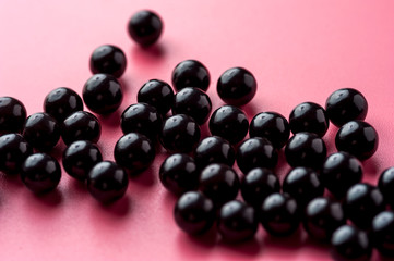 Close-up of black shiny pills lie on a pink surface