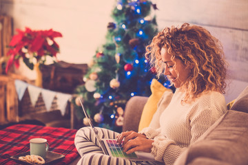 woman alone at home sitting on the sofa working or shopping with laptop and with cookies and tea or...