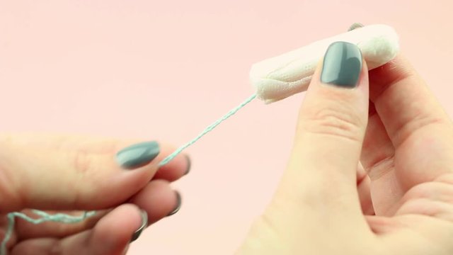 Close up of woman hand holding menstruation cotton tampon on pink background. Feminine hygiene product.