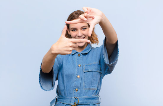 young blonde woman feeling happy, friendly and positive, smiling and making a portrait or photo frame with hands against flat color wall