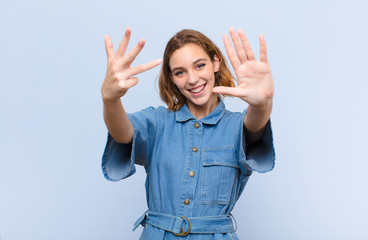 young blonde woman smiling and looking friendly, showing number nine or ninth with hand forward,...