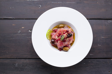 Top view tuna carpaccio on a big white plate of Italian recipe with olive oil, spices and lime...