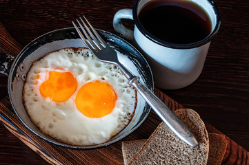 Fried scrambled eggs in vintage pan, with bread, old fork, metal mug with tea, top view, close-up