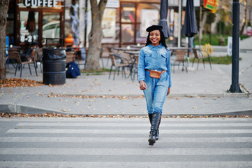 Stylish fashionable african american women in jeans wear and black beret walking on pedestrian traffic.