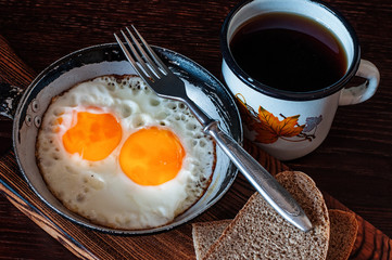 Fried scrambled eggs in vintage pan, with bread, old fork, metal mug with tea, top view, close-up