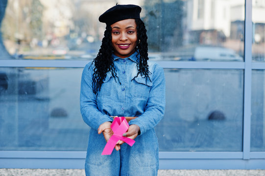 The power to fight. Stylish fashionable african american women in jeans wear and black beret against modern building with pink ribbon for breast cancer.