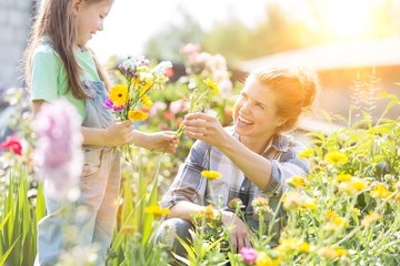 Smiling mother giving flowers to daughter while gardening at farm