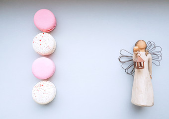 Pattern of pink and cream macaroons   and an angel handmade figurine with a candlestick. A minimalist concept for a congratulation on holidays. Copy space.