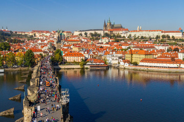 Fototapeta premium City views Prague autumn. Tiled roofs. The Charles Bridge. Vlatva river. People and Harvesting Equipment. View from above.