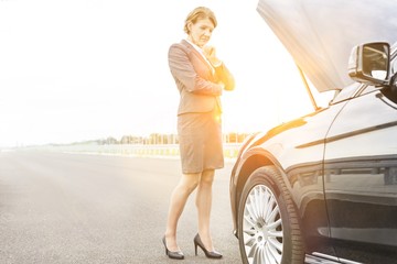 Obraz na płótnie Canvas Mature businesswoman looking at breakdown car on road