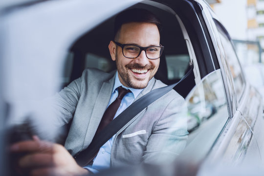 Cheerful caucasian businessman driving himself to work. Hands are on steering wheel.