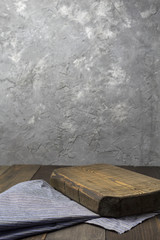 An old wooden tabletop against a blurred concrete wall. On the table is an old cutting Board with a napkin. The layout for the design. The vertical format.